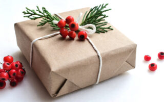 holiday office gift giving etiquette | Christmas gift wrapped in brown paper, adorned with fresh greenery and berries