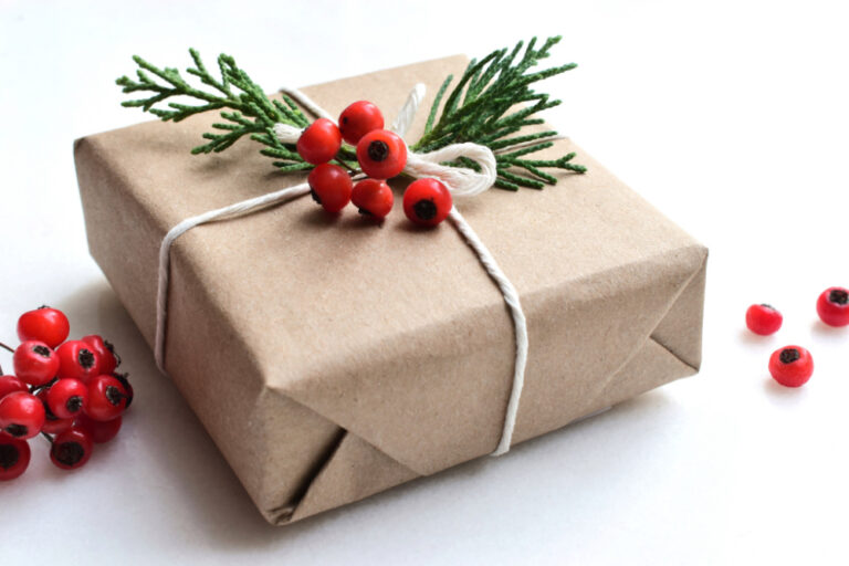 holiday office gift giving etiquette | Christmas gift wrapped in brown paper, adorned with fresh greenery and berries