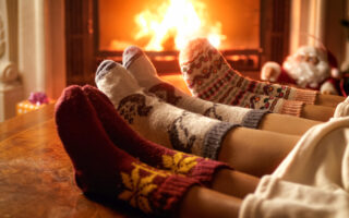 holiday traditions | close up of holiday socks on three people sitting near the fireplace