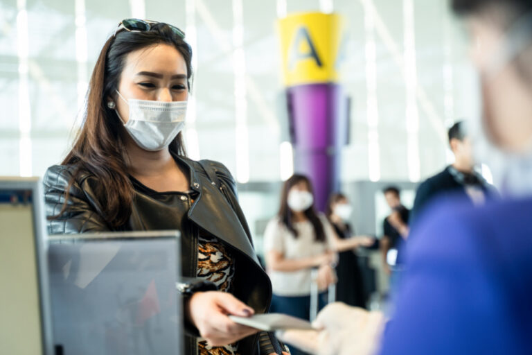 Post-Pandemic Travel Etiquette | woman wearing mask, handing passport to attendant in airport