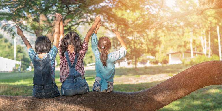 National Friendship Month | Children sitting on tree branch, arms on one another's backs
