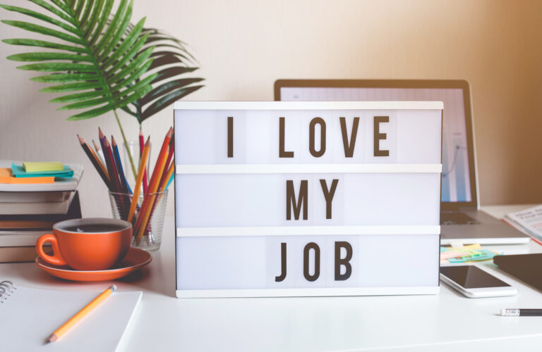 psychological safety | lightbox sign that reads "I Love My Job" on top of a desk with a computer, jar of pencils and a cup of coffee