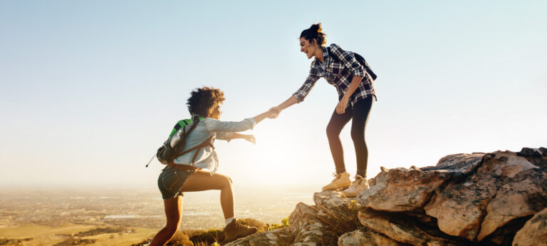strengthen relationships by showing up | one woman helping another woman up on a hike
