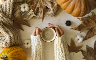 ideas for fall | woman's hands in white sweater, holding cup of pumpkin spice coffee next to leaves and a pumpkin