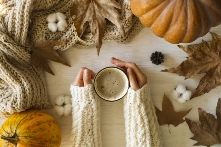 ideas for fall | woman's hands in white sweater, holding cup of pumpkin spice coffee next to leaves and a pumpkin