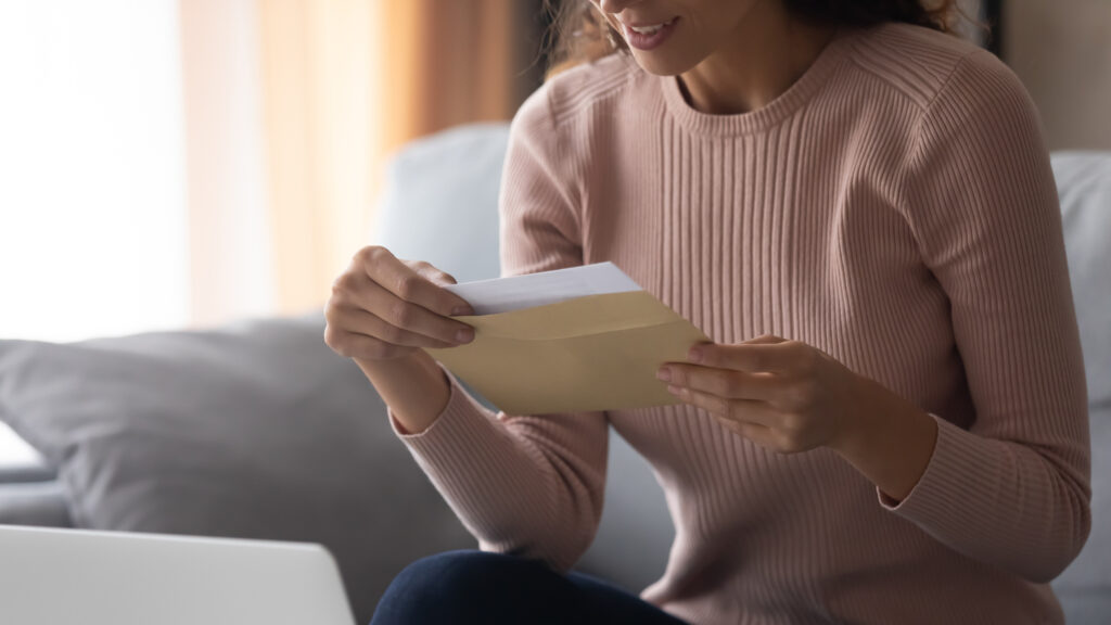 thank you note | woman opening card, wearing blush sweater, sitting down