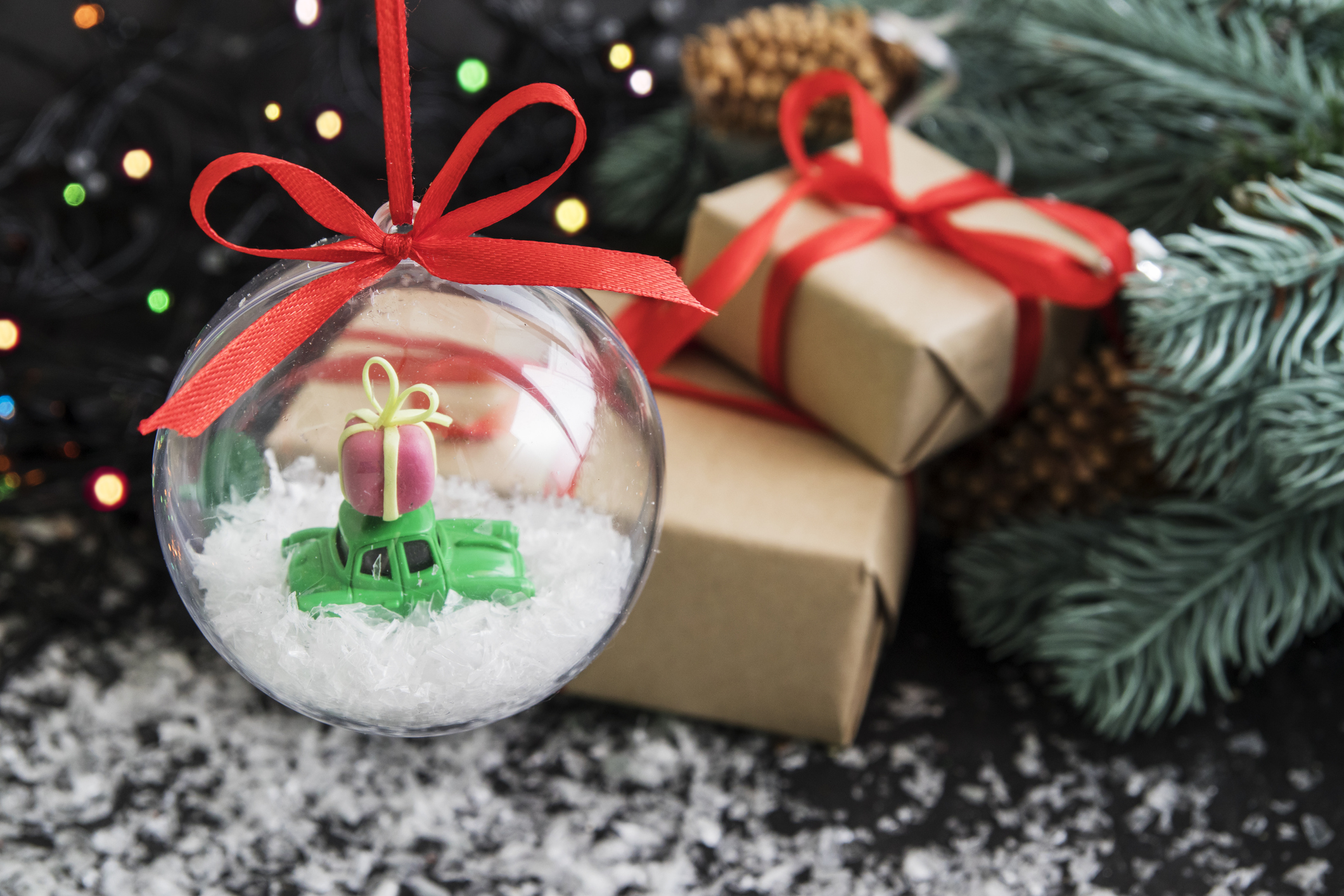 road trip must-haves | Transparent christmas ball with toy car and gift box on dark background with colored lights