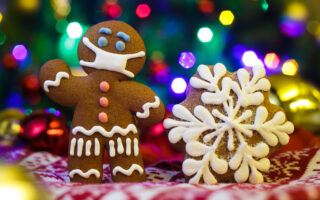 unvaccinated guests | gingerbread man wearing a mask made of frosting, holiday lights in the background, snowflake cookie nearby