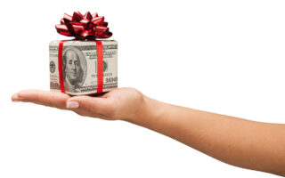 2021 Holiday Tipping Guide | Woman's hand extended with bills in the shape of a house, tied with a red ribbon