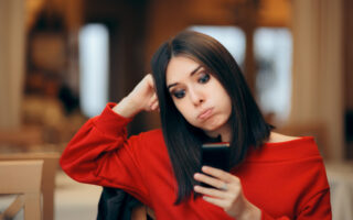 How Much Time Do You Have To Respond to a Text? | Woman in red shirt looking at her phone with a disappointed look on her face