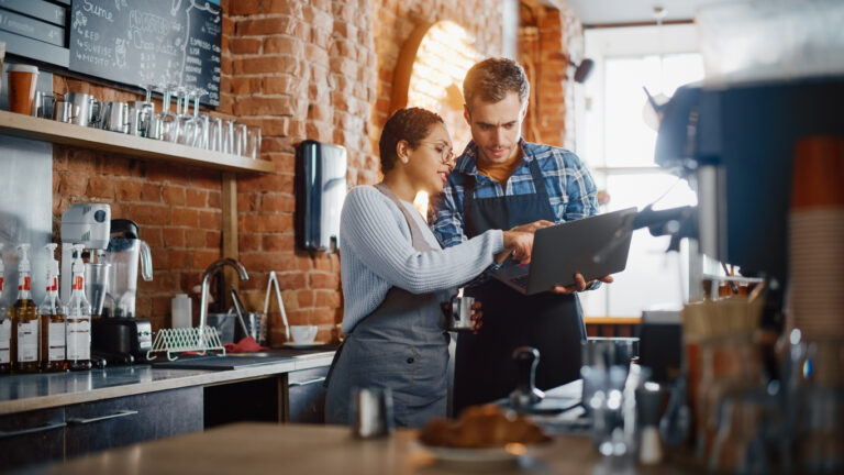 employee happiness | Two Diverse Entrepreneurs Have a Team Meeting in Their Stylish Coffee Shop. Barista and Cafe Owner Discuss Work Schedule and Menu on Laptop Computer. Multiethnic Female and Male Restaurant Employees.