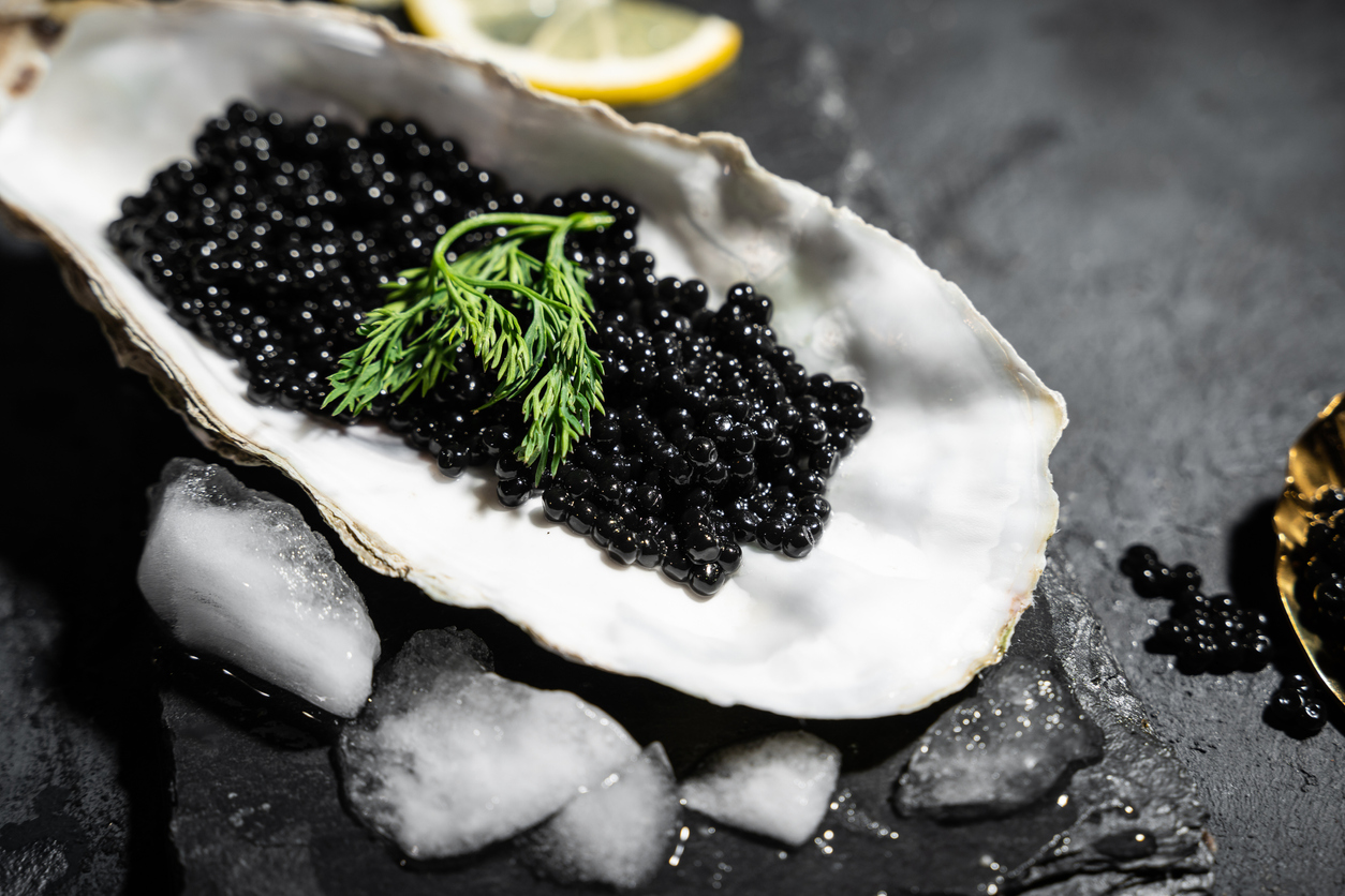 how to eat caviar etiquette | Black caviar in oyster shell on black slate background