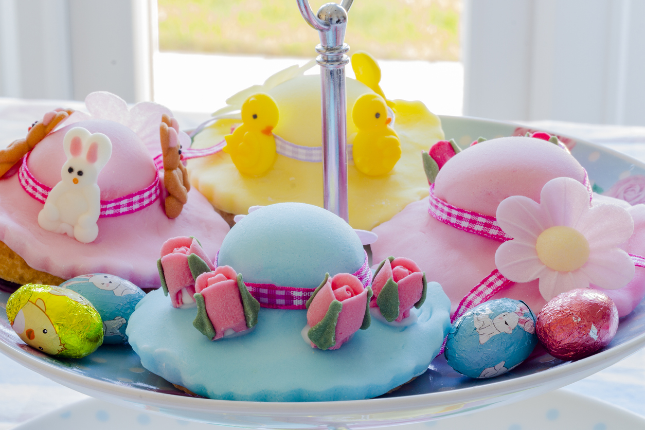 Baked Easter bonnet biscuits, pastel shades of pink, blue and lemon with ribbons and decorations for Easter tea.