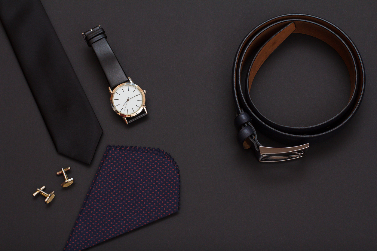 Graduation gift ideas | Silk tie, watch with a black leather strap, cufflinks, handkerchief and leather belt with metal buckle on black background. Accessories for men. Top view.