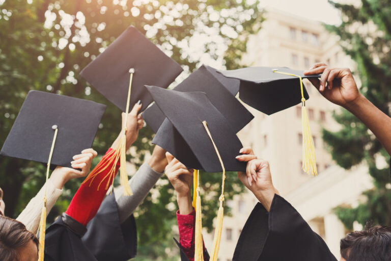 graduation gift ideas | A group of multietnic students celebrating their graduation by throwing caps in the air closeup. Education, qualification and gown concept.