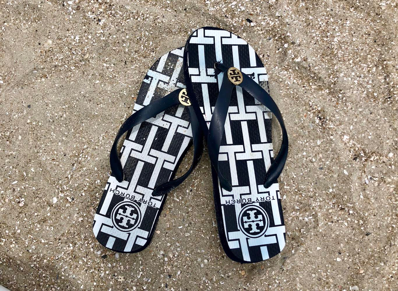 black and white flip flops on a sandy beach