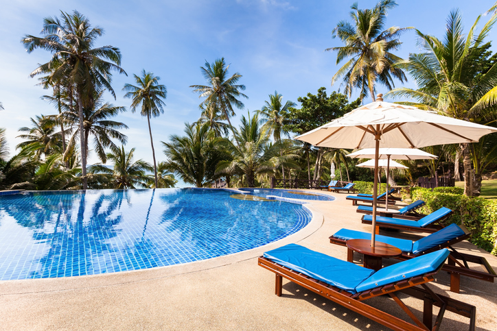 2022 Summer Travel Etiquette | Beautiful tropical beach front hotel resort with swimming pool, sun-loungers and palm trees during a warm sunny day, paradise destination for vacations