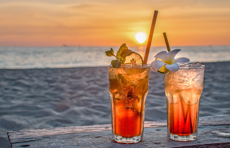 Travel Etiquette Q & As | drinks with blur beach and sunset in background