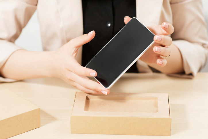 Female hands holding new smartphone. Customer taking gadget from post package. Recent model of phone delivery