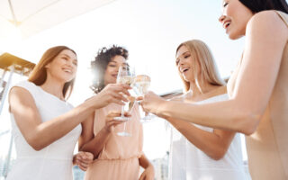 Bachelorette Party Etiquette Q & | Joyful happy young women standing together and cheering with champagne while having a celebration