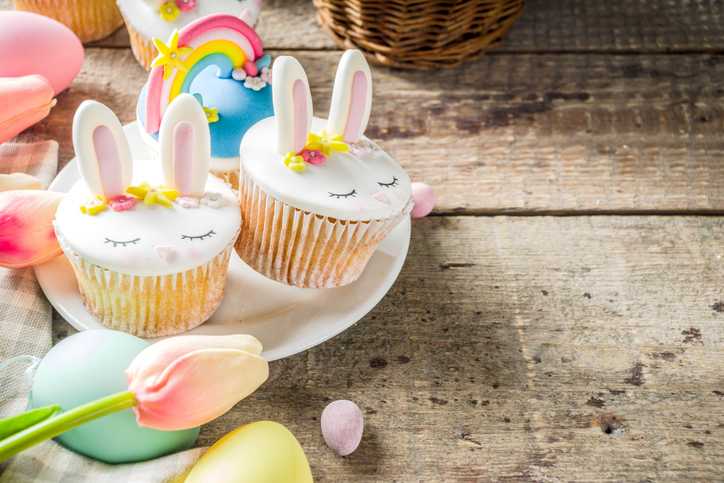 Easter holiday greeting card background. Cute homemade cupcakes with traditional Easter bunny, egg and springtime flowers decor. Happy easter concept. Copy space for your text