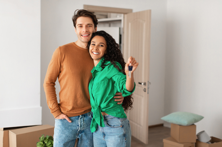 saving for your first home | House Ownership. Portrait Of Happy Young Couple Holding Showing Key Standing In New Flat, Cheerful Guy Embracing Lady Posing After Moving In Own Apartment. Insurance, Real Estate, Mortgage Concept