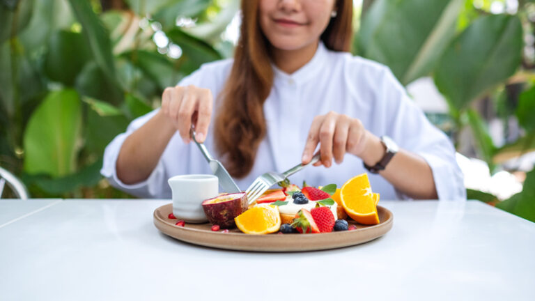 Table manners for teens | Closeup of a young woman eating mixed fruits french toast brunch in restaurant