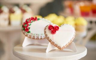 bridal shower etiquette Q&A | Round and heart shaped glazed cookies, decorated with glaze flowers and pattern are on the wooden stand in the restaurant. There is a colorful delicious candy bar behind them.