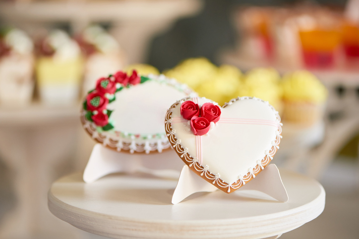 bridal shower etiquette Q&A | Round and heart shaped glazed cookies, decorated with glaze flowers and pattern are on the wooden stand in the restaurant. There is a colorful delicious candy bar behind them.