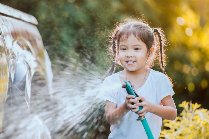 Happy asian child girl help parent washing car on water splashing with sunlight