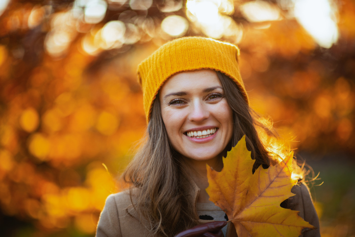 how to have a fall "glow up" Hello october. smiling 40 years old woman in beige coat and orange hat with autumn yellow leaves outdoors in the city park in autumn.