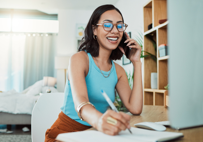 Creative entrepreneur talking on business phone call, writing in notebook and planning a project working remote at house. Happy, learning and young woman doing freelance and making notes in book