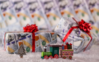 2023 Holiday tipping guide | Toy wood train and gifts wrapped in wrapping paper with american dollars