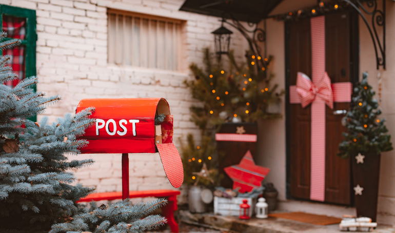 Festive Christmas decoration of the facade of the house in the new year. Red retro mailbox for Santa greetings on the background of the porch door with a large bow. Xmas 2022