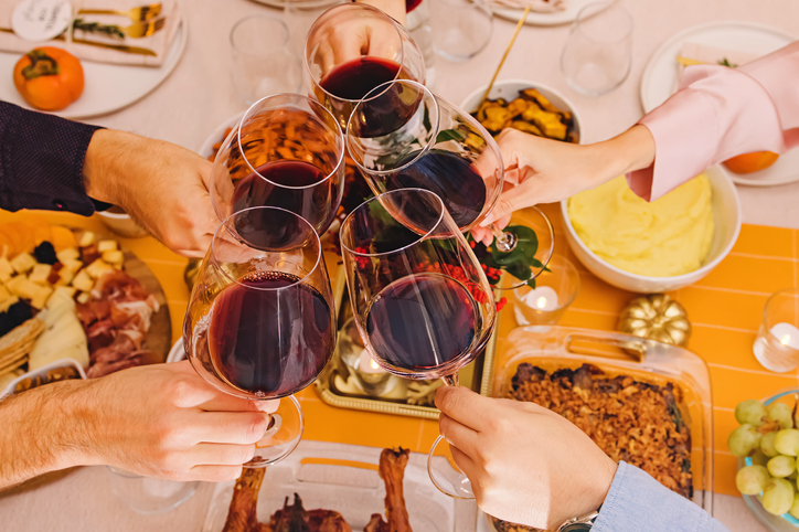 Hands clinking with a glasses filled with red wine at the Thanksgiving dinner table. Celebration, gather, Friendsgiving