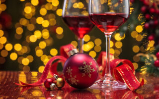 holiday party etiquette | Red wine in wineglasses and Christmas ball against holiday lights background.