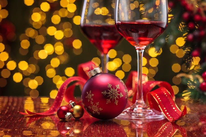 holiday party etiquette | Red wine in wineglasses and Christmas ball against holiday lights background.