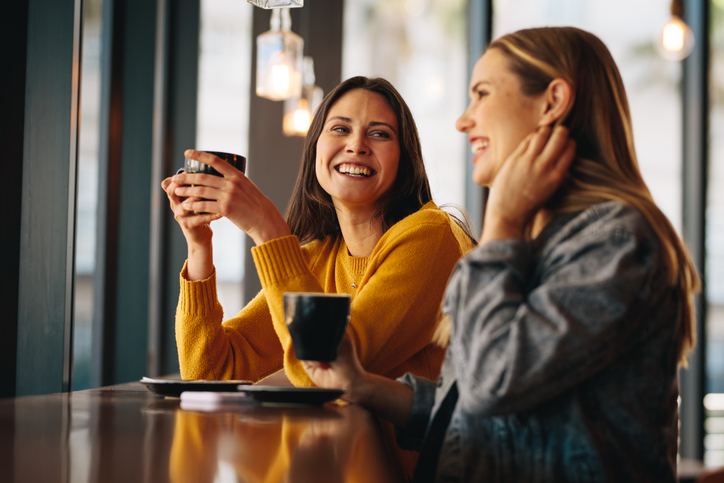 Two female friends sitting at cafe having coffee and gossiping. Female friends meeting in a coffee shop on a weekend.