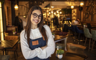 Restaurant Etiquette | Portrait of a confident young woman standing in the doorway of a coffee shop. Portrait of Smiling cafeteria owner. Small business owner at entrance looking at camera