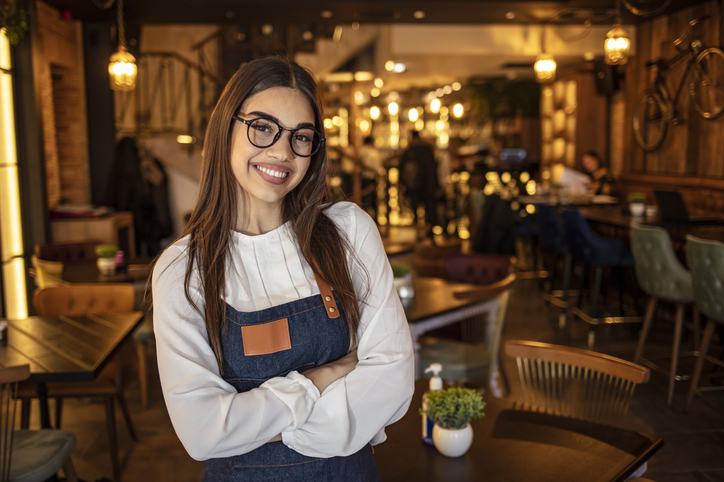Restaurant Etiquette | Portrait of a confident young woman standing in the doorway of a coffee shop. Portrait of Smiling cafeteria owner. Small business owner at entrance looking at camera