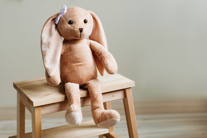 Kids soft toy rabbit with bow sitting on the wooden kids chair in children room. Selective focus.