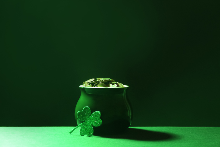 Pot of gold coins and clover on green table against dark background. St. Patrick's Day celebration