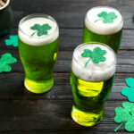 St. Patrick's Day Party Etiquette | Green beer and clover leaves on black wooden table. St. Patrick's Day celebration