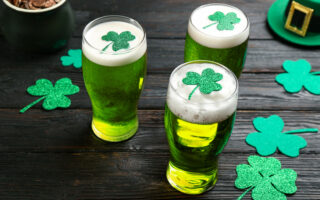 St. Patrick's Day Party Etiquette | Green beer and clover leaves on black wooden table. St. Patrick's Day celebration