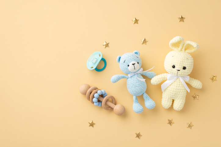 Easter Luncheon Etiquette | Baby accessories concept. Top view photo of knitted bunny and teddy-bear toys wooden rattle blue pacifier and gold stars on isolated pastel beige background with copyspace