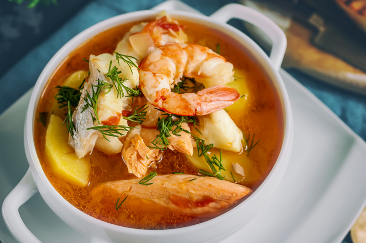 French fish soup Bouillabaisse with seafood, salmon fillet, shrimp, rich flavor, delicious dinner in a white beautiful plate. Close up.