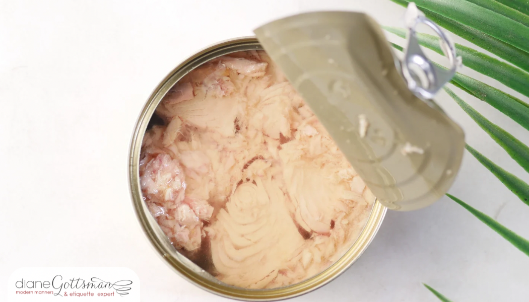 Etiquette of eating tuna on a flight | can of tuna opened on white background with leaves on right side