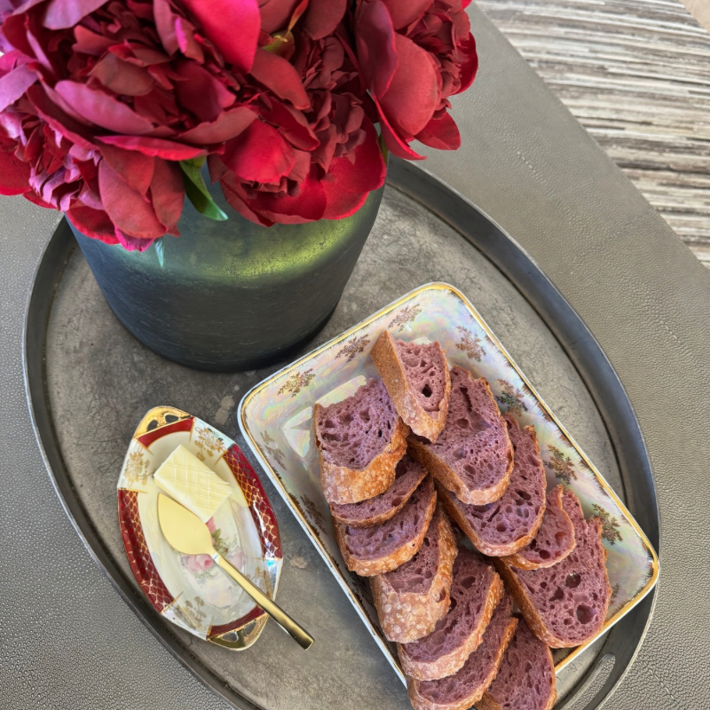 Plate of sourdough bread next to butter dish and flowers in vase