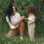 Mother’s Day Etiquette Q&A - Mother and child in lush outdoor field, dressed in neutral colors with curly/wavy hair