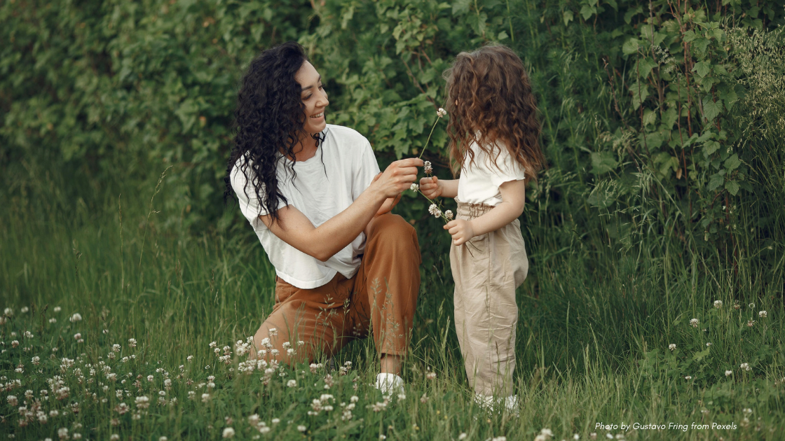 Mother’s Day Etiquette Q&A - Mother and child in lush outdoor field, dressed in neutral colors with curly/wavy hair